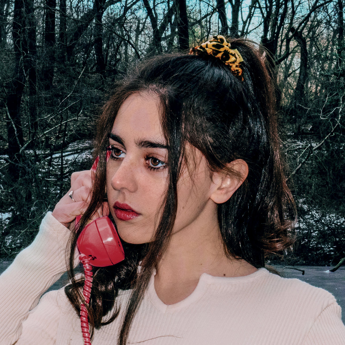 Samia mit rotem Telefon in der Hand, träumerisch und verletzlich vor einem winterlichen Wald