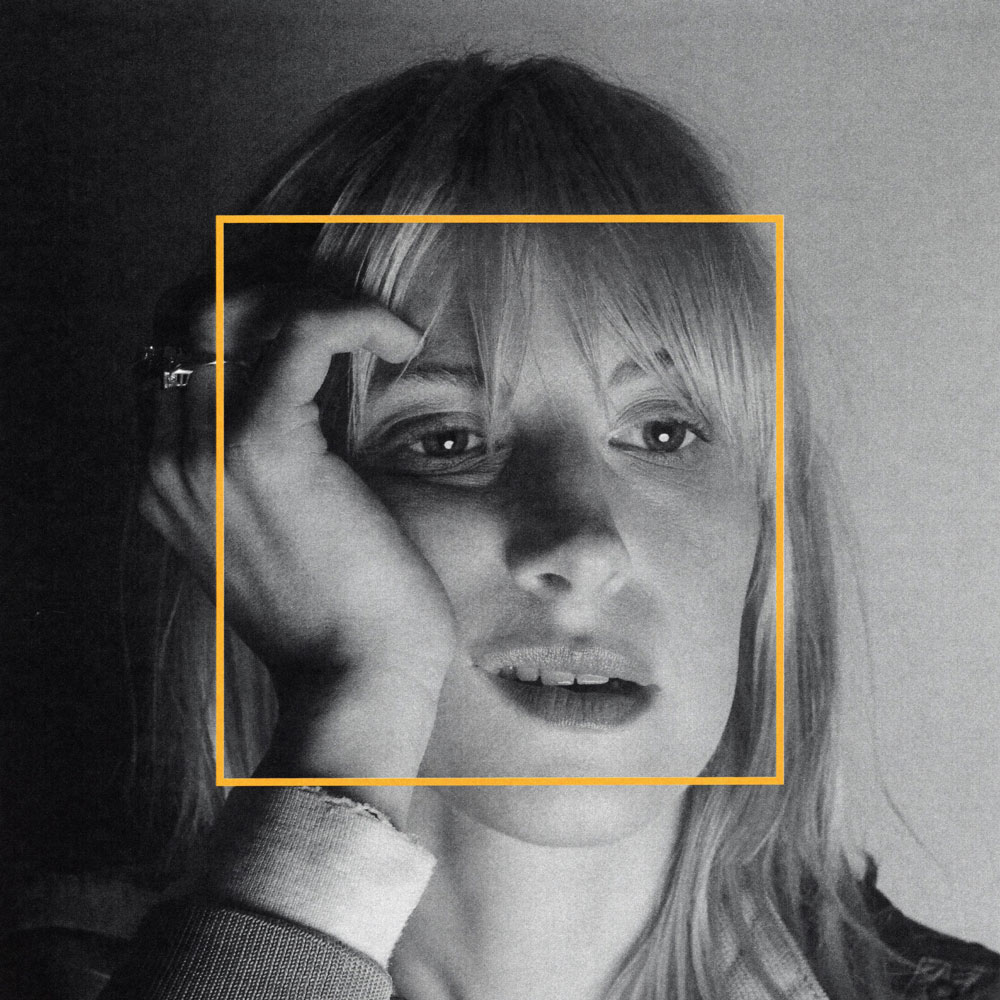Schwarz-weißes Close-up von Hayley Williams, Blick zur Seite, Hand an der Schläfe, ein gelbes Quadrat markiert das Gesicht wie ein Rahmen, körnige Textur, ruhige Lichtkante.