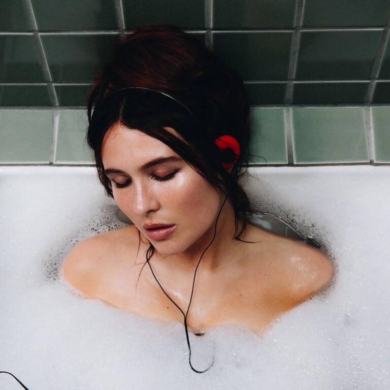 Mimi Webb liegt mit geschlossenen Augen in einer Badewanne voller Schaum, gekachelt von graugrünen Fliesen umrahmt, ein intimes und nachdenkliches Covermotiv.
