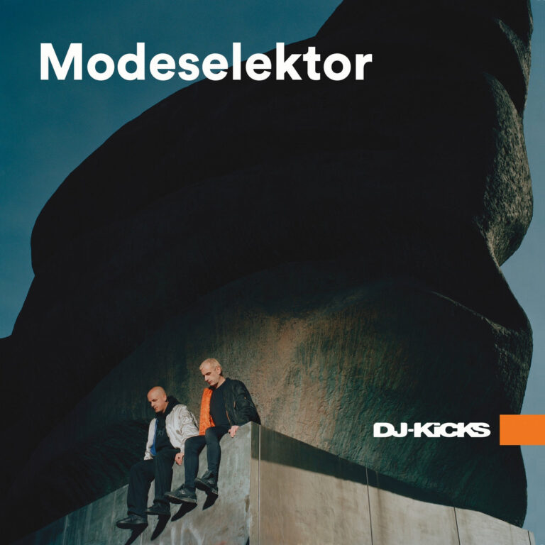 Zwei Männer sitzen auf einem kantigen Vorsprung vor einer massiven dunklen Felsstruktur, im Hintergrund blauer Himmel, darüber weiß der Schriftzug „Modeselektor“ und unten „DJ-Kicks“.