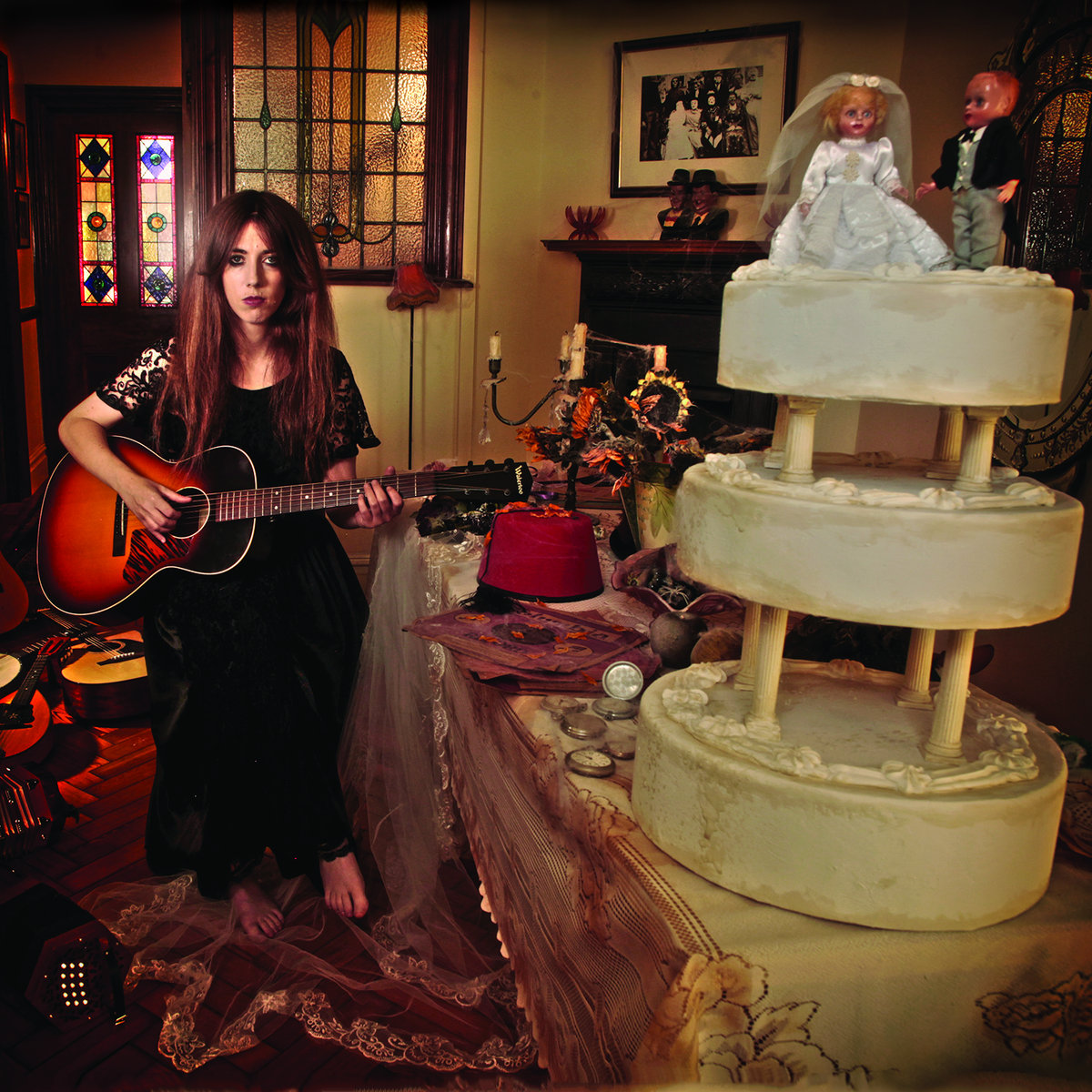 Eine Frau mit Gitarre sitzt barfuß neben einer prunkvollen Hochzeitstorte, im Raum Kerzen, Blumen und viktorianische Details, Atmosphäre zwischen Folk und Gothic.