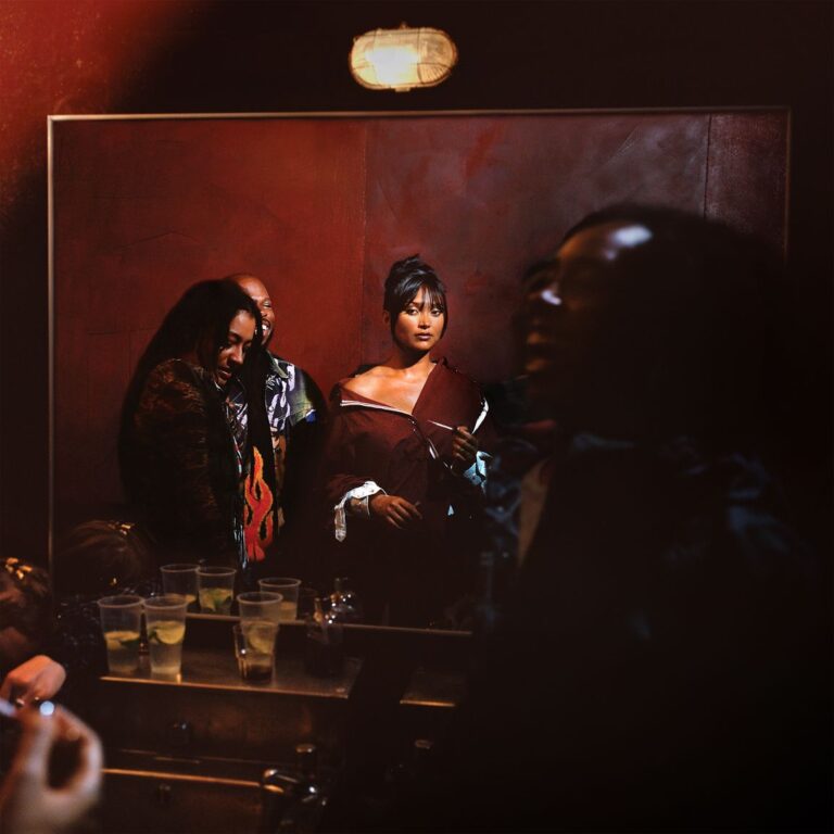 Joy Crookes im Spiegelbild vor roter Wand, umgeben von weiteren Personen, halb im Schatten, auf einem Cover mit nächtlicher, geheimnisvoller Atmosphäre.