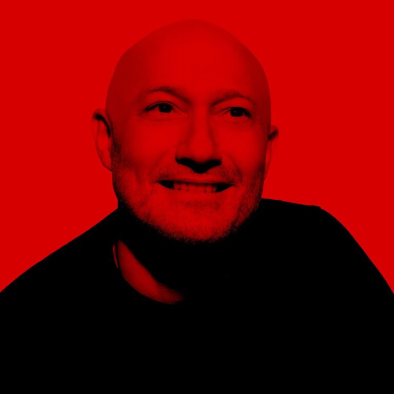 Porträt von Paul Kalkbrenner vor rotem Hintergrund, das Gesicht halb im Schatten, halb im Licht, symbolisch für die innere Spannung seines Albums „The Essence“.