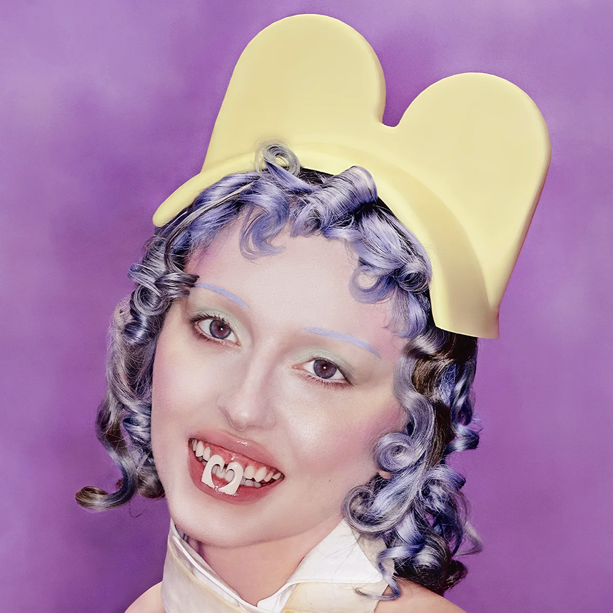 Porträtiertes Gesicht mit violett getönten Locken, gelbem Kopfschmuck und surrealem Zahnschmuck vor lila Hintergrund, poppig und künstlich inszeniert.