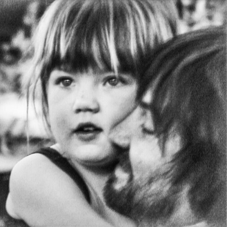 Schwarzweißfotografie mit einem Mann, der ein kleines Kind im Arm hält. Weiche Kontraste, zarte Lichtstimmung, intime Nähe zwischen den beiden Personen, leicht unscharfer Hintergrund.