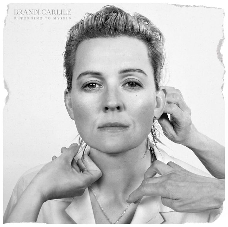 Schwarzweiß-Porträt von Brandi Carlile mit ernstem Blick, mehrere Hände berühren ihr Gesicht und ihren Hals, reduzierter Hintergrund, starke Lichtkontraste.