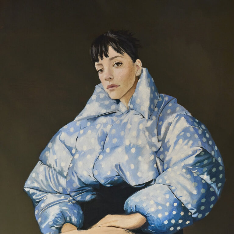 Porträt einer Frau mit dunklem Haar in hellblauer, gepunkteter Steppjacke vor dunklem Hintergrund. Ihr Blick wirkt ruhig, fast abwesend, das Licht modelliert sanft Gesicht und Stoff.