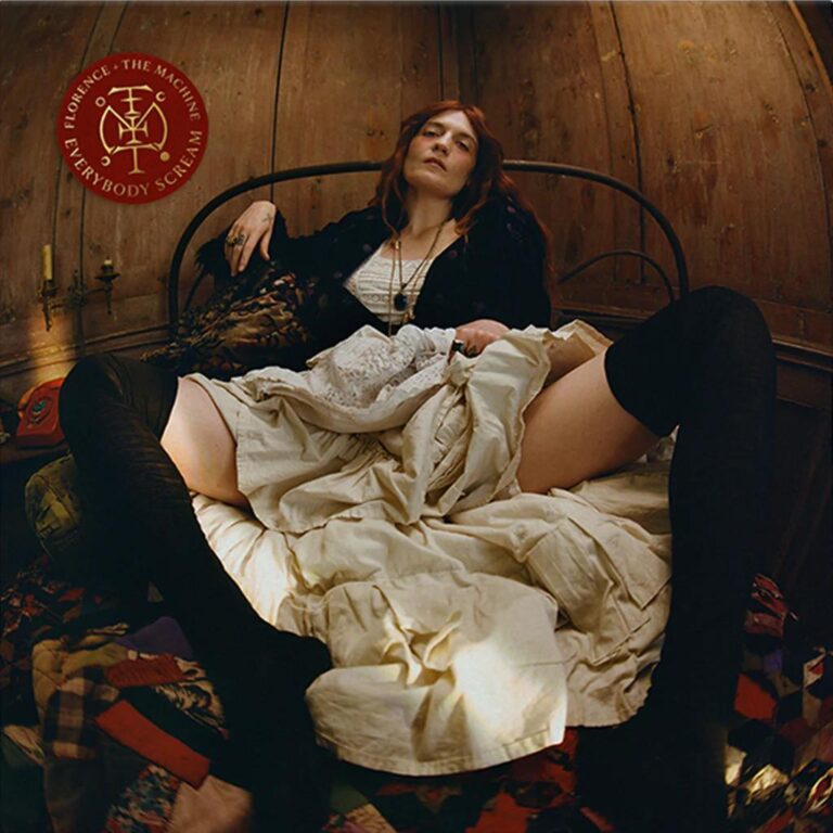 Florence Welch liegt in einem engen Holzraum auf einem Bett, halb aufgerichtet, halb erschöpft, in weißem Kleid und schwarzen Strümpfen, Blick nach oben, zwischen Ritual und Rückzug.
