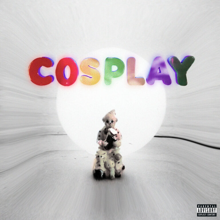 Eine weiße Fläche mit einem hellen Lichtkreis, darüber in bunten Lettern der Schriftzug „COSPLAY“. Im Vordergrund sitzt eine kleine Figur mit Clownsmaske und melancholischem Ausdruck, umgeben von diffuser Helligkeit.