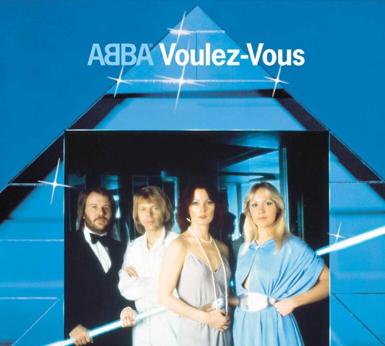 Vier Mitglieder von ABBA stehen vor einer blau beleuchteten, geometrischen Studio-Kulisse mit spiegelnden Flächen, hartem Licht, klaren Reflexen. Die Szene wirkt wie ein künstlich inszenierter Nachtclubraum, die Farbigkeit kühl, die Komposition streng symmetrisch.