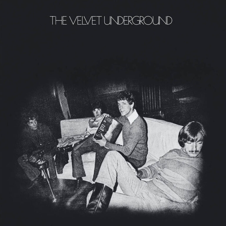 Schwarzweiß Fotografie von The Velvet Underground 1969. Vier Bandmitglieder sitzen ruhig auf einer Couch in der Factory. Gedämpftes Licht, grauer Hintergrund, distanzierte Atmosphäre.