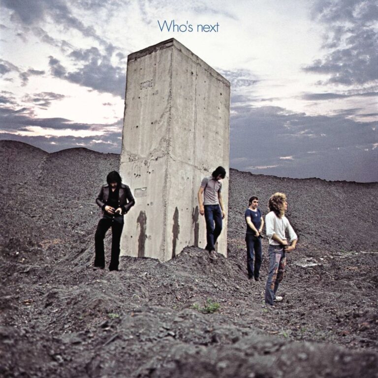 Vier Mitglieder von The Who stehen vor einem massiven Betonpfeiler in einer grauen Industriebrache unter wolkenverhangenem Himmel.
