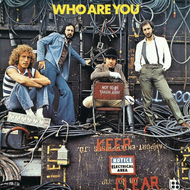 Vier Bandmitglieder von The Who stehen und sitzen vor einer Wand aus Kabeln und Technik, umgeben von Warnschildern, industrieller Umgebung und dem Schriftzug „Who Are You“.