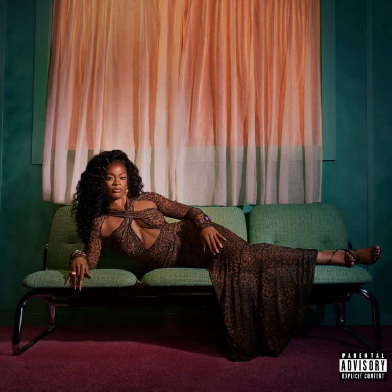 Ari Lennox liegt selbstbewusst inszeniert auf einem Sofa in einem stilisierten Raum mit Vorhängen und gedämpften Farben, das Albumcover zu „Vacancy“.