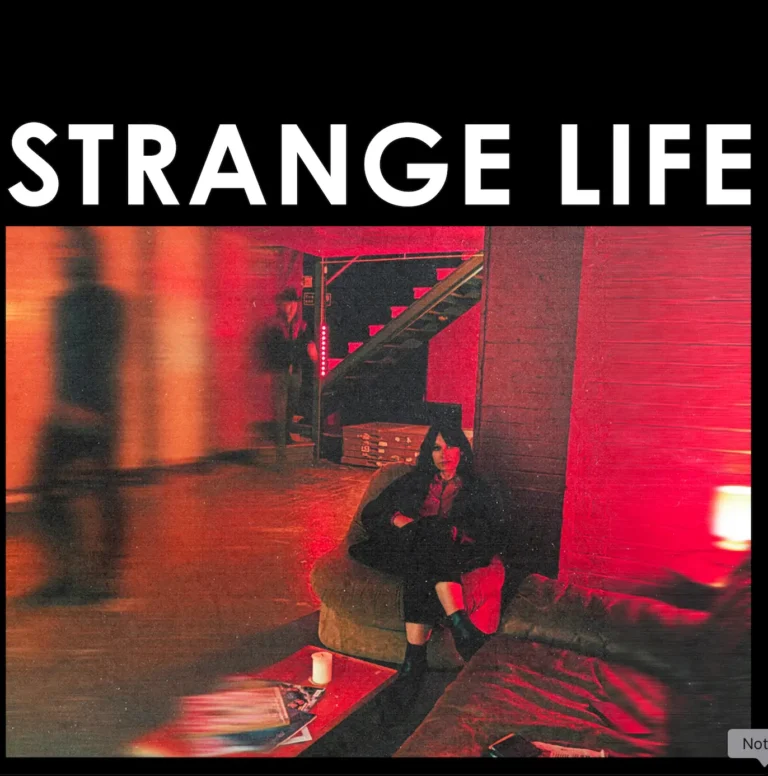 Howling Bells sitzen in einem rot ausgeleuchteten Kellerraum, Juanita Stein im Vordergrund mit verschränkten Armen, unscharfe Figuren im Hintergrund.