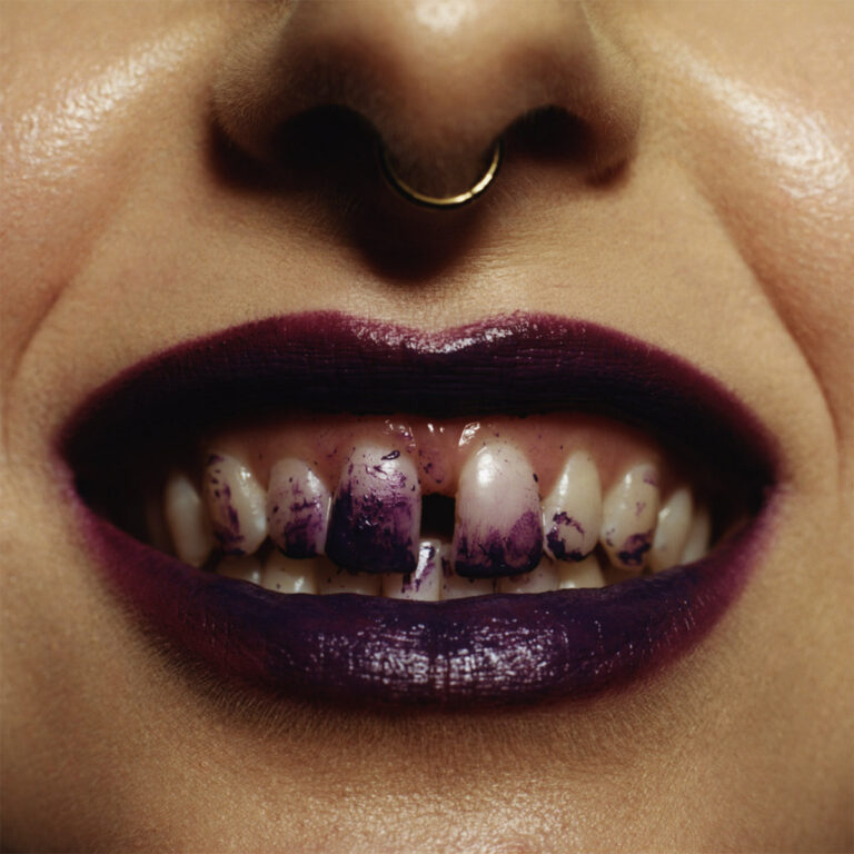 Nahaufnahme eines Mundes mit dunklem Lippenstift, lila verfärbten Zähnen und Septumring als provokante, kunstvolle Inszenierung.