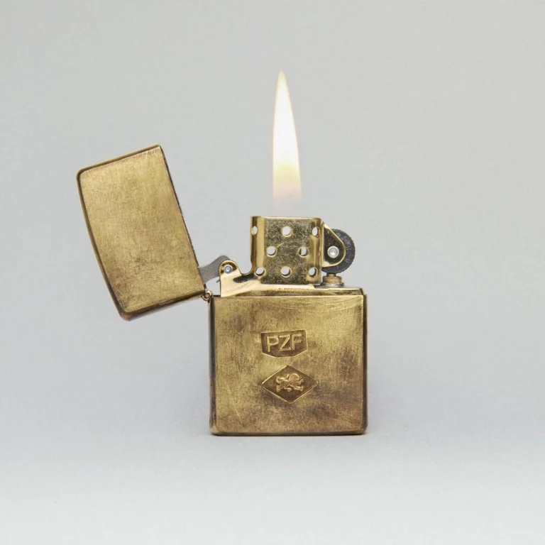 Goldenes Zippo-Feuerzeug mit Flamme vor neutralem Hintergrund.