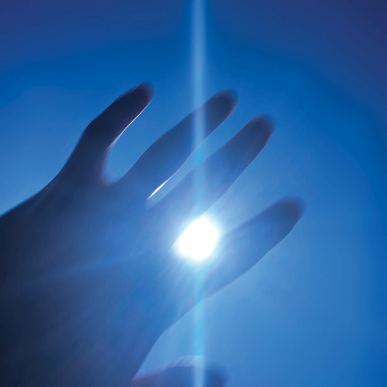 Eine Hand vor gleißendem Licht in kühlem Blau, die Sonne scheint durch die Finger und erzeugt eine diffuse, entrückte Atmosphäre.