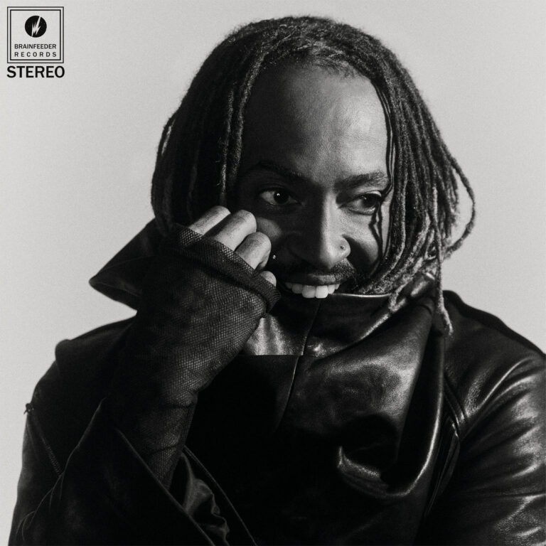 Das Schwarz-Weiß-Foto zeigt Thundercat in einer Nahaufnahme. Er trägt eine schwarze Lederjacke mit hohem Kragen und schwarze Netzhandschuhe. Sein Gesicht ist halb hinter dem Kragen und seiner Hand verborgen, während er lächelt und zur Seite blickt. Seine Dreadlocks rahmen sein Gesicht ein. Oben links befinden sich das Logo von Brainfeeder Records und der Schriftzug „STEREO“.