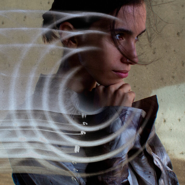 Das quadratische Albumcover zeigt das Porträt einer Person im Profil vor einem beigen, strukturierten Hintergrund. Über das Gesicht und den Oberkörper legen sich helle, halbtransparente, spiralförmige Lichtstreifen, die an eine glühende Herdplatte erinnern und das Bild optisch verzerren.