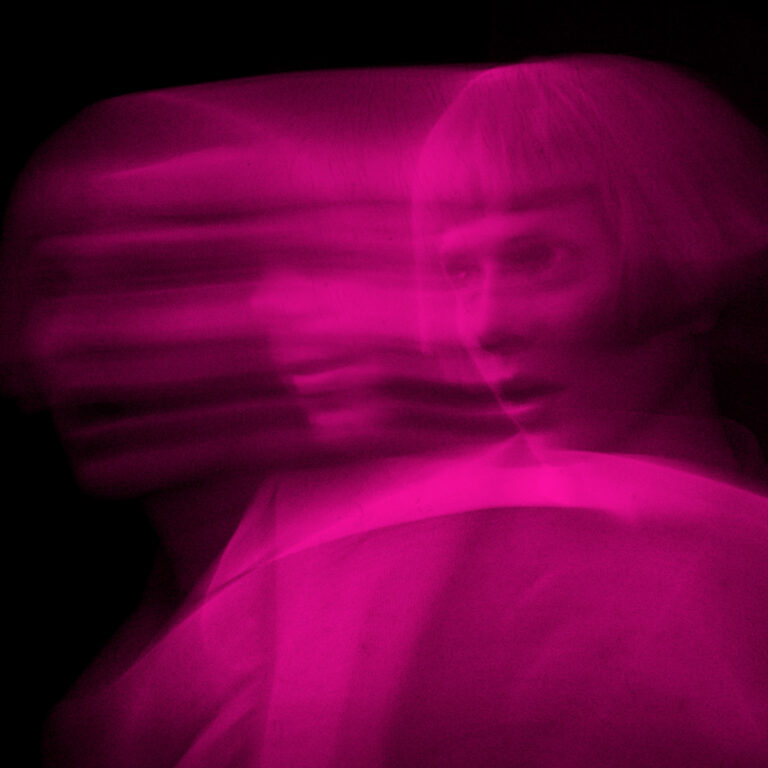 Ein minimalistisch gestaltetes Porträt von Aurora in futuristischer, stark stilisierter Ästhetik vor einem dunklen, technoiden Hintergrund, das eine Atmosphäre von unterkühlter Eleganz und künstlicher Distanz vermittelt.