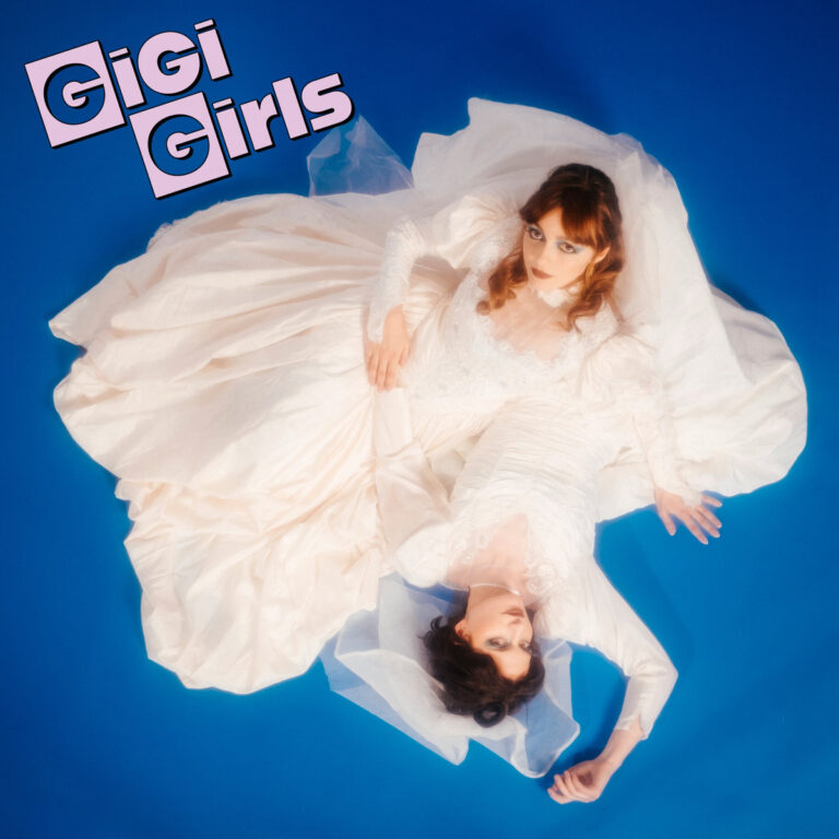 Das Beitragsbild zeigt das Trio GiGi Girls in einer stilisierten 80er-Jahre-Ästhetik vor einem weichgezeichneten Hintergrund, wobei Laura Mancini im Zentrum steht und die Bandmitglieder in theatralen Posen und zeittypischen Kostümen eine nostalgische Italo-Pop-Atmosphäre evozieren.