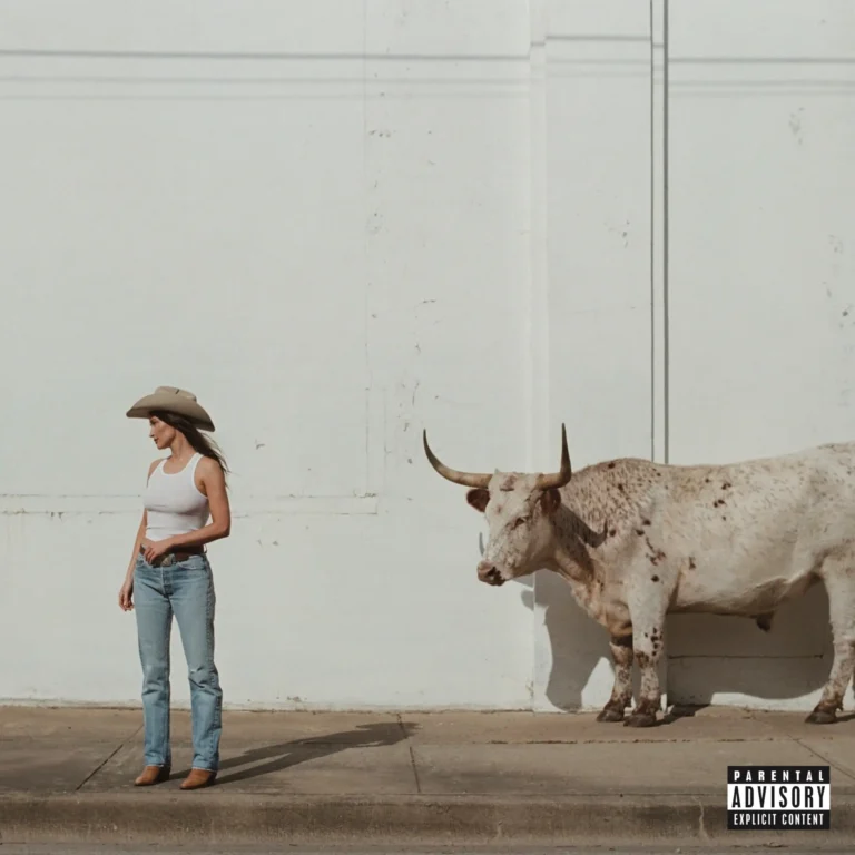 Kacey Musgraves steht in einem weißen Tanktop, blauen Jeans und einem Cowboyhut auf einem Gehweg vor einer hohen, weiß getünchten Wand. Rechts neben ihr steht ein großes, helles Texas-Longhorn-Rind mit weiten Hörnern und dunklen Flecken. Die Komposition ist minimalistisch und hell, im rechten unteren Eck befindet sich ein „Parental Advisory“-Hinweis.