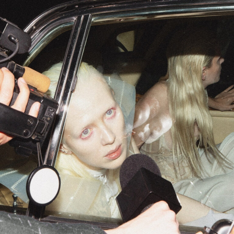 Blonde Frau im Auto blickt inmitten von Paparazzi-Mikrofonen und Kameras direkt nach draußen.