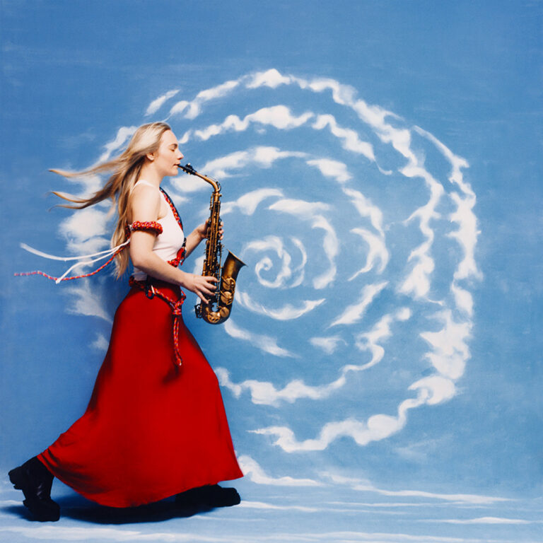 Eine junge Frau im roten Rock spielt Saxophon vor einem wolkenverzierten blauen Hintergrund
