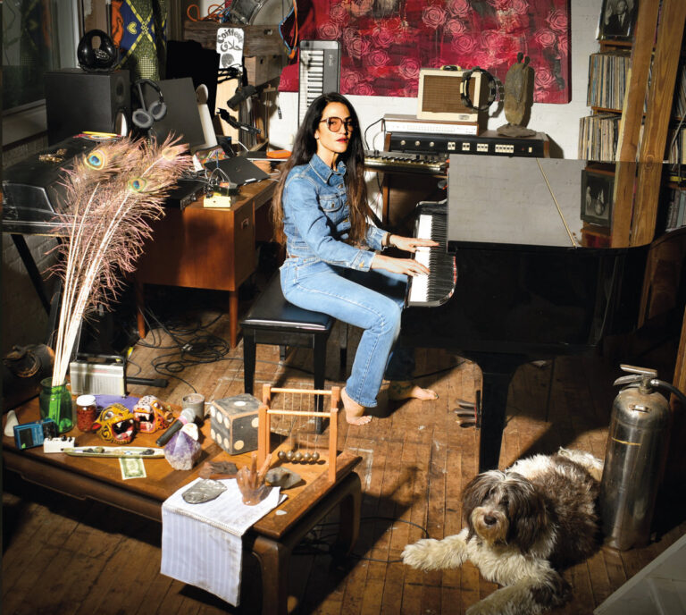 Joan Wasser sitzt im Denim-Outfit an einem schwarzen Flügel in einem detailreichen Musikzimmer.