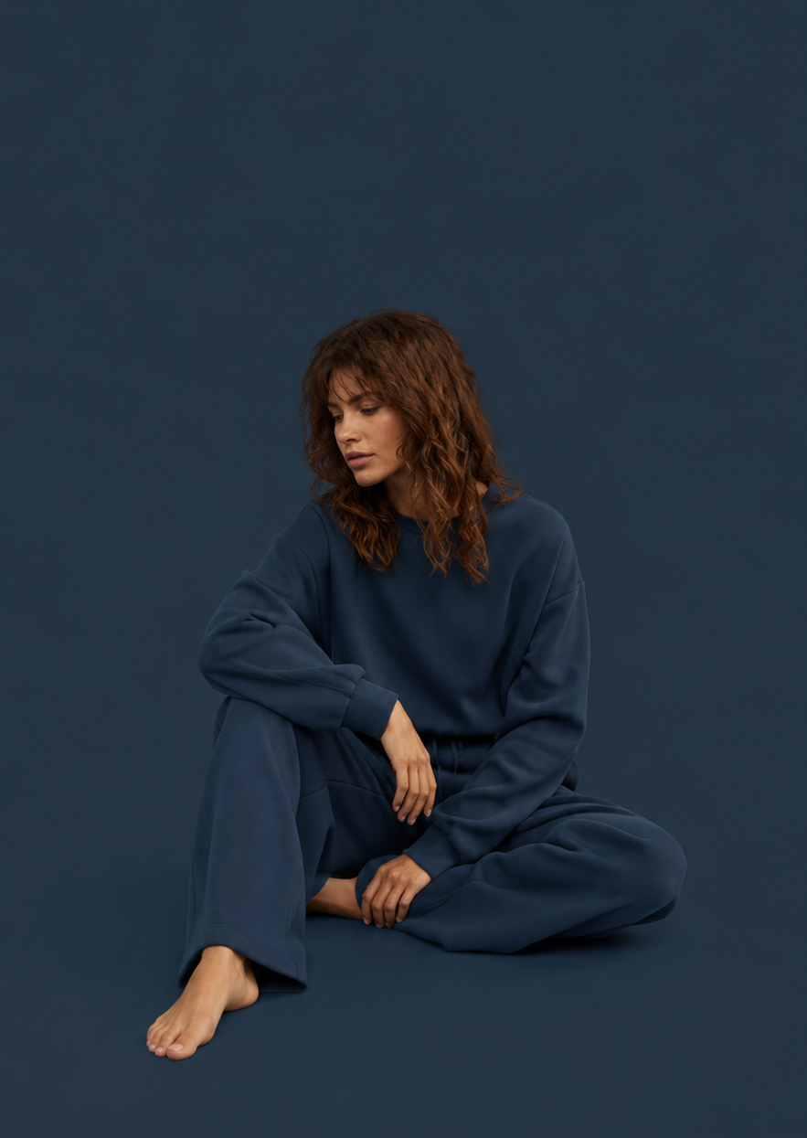 Eine junge Frau in monochromem blaugrauem Outfit sitzt nachdenklich vor einem gleichfarbigen Hintergrund und verkörpert die stille Atmosphäre der Melancholie.