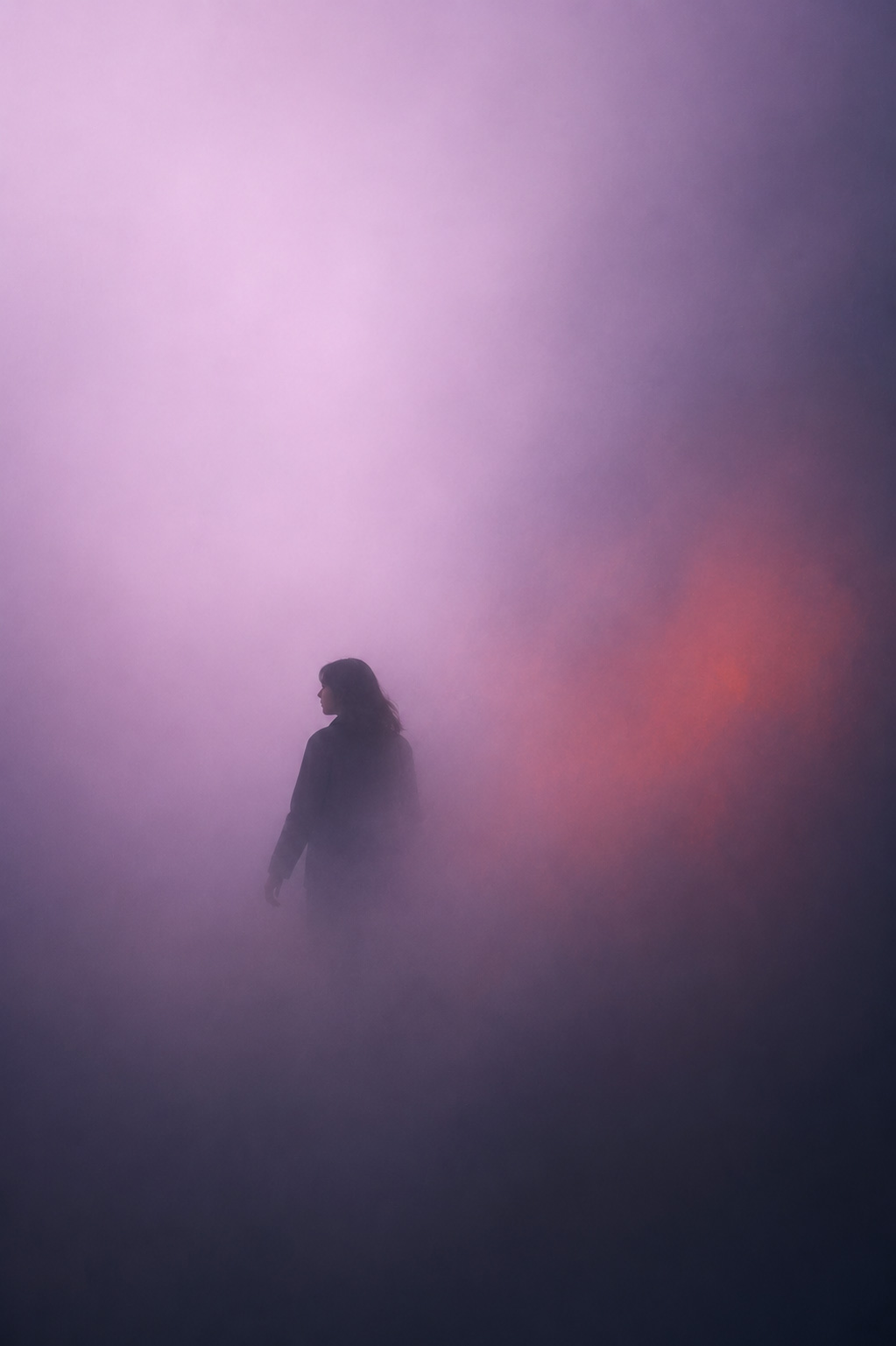 Eine einsame Gestalt bewegt sich durch eine dichte Wand aus lavendelfarbenem Nebel, deren Konturen sich ständig verschieben und jede Orientierung erschweren. Zwischen sanften Lichtspuren und dunklen Schattenzonen entsteht das Gefühl eines vorsichtigen Voranschreitens durch eine Welt, die mehr verbirgt als preisgibt.