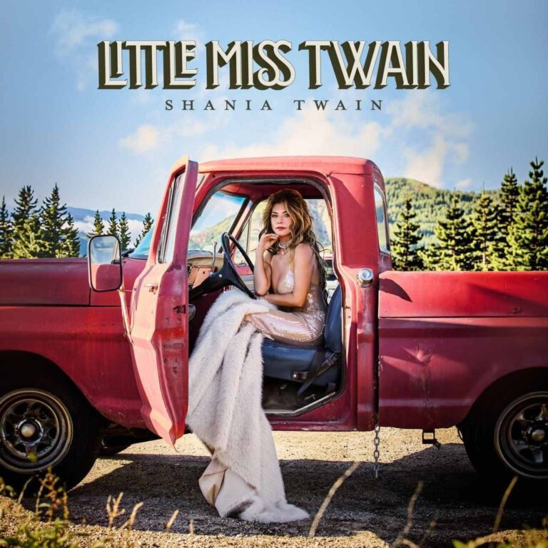 Shania Twain sitzt im Abendkleid auf dem Fahrersitz eines alten roten Pick-ups.