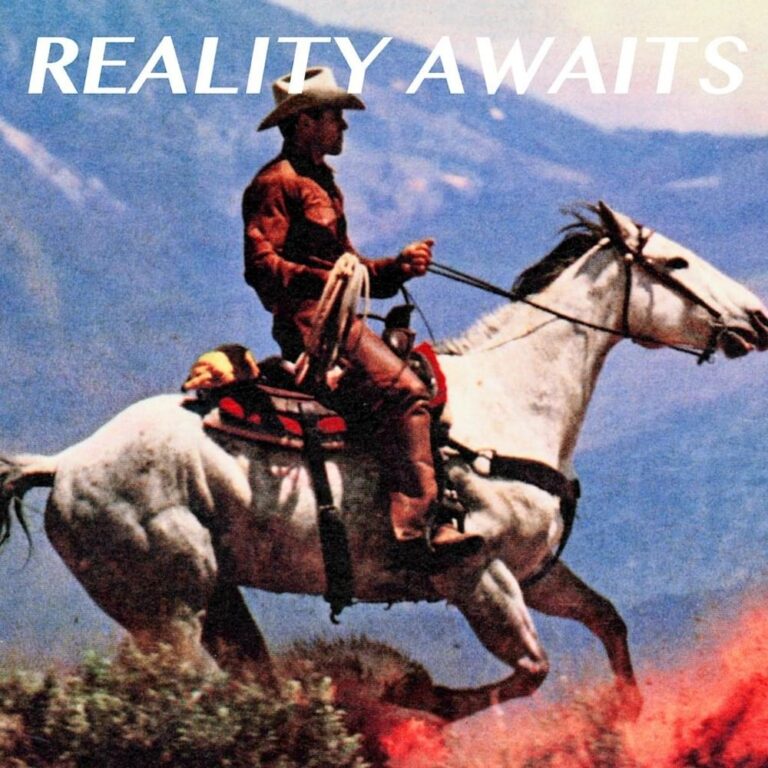 Ein Cowboy auf einem Schimmel reitet vor einer Bergkulisse durch die Landschaft.
