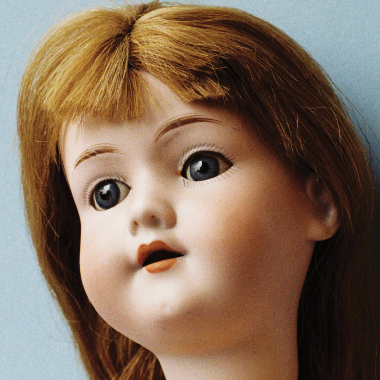 Porträt einer antik wirkenden Porzellanpuppe mit brünettem Haar und blau blickenden Augen.