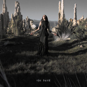 Chelsea Wolfe steht in einem schwarzen Kleid in einer steinigen Landschaft.