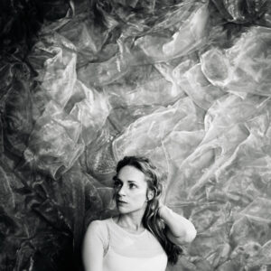 Agnes Obel liegt im hellen Licht auf geknitterter Folie und blickt nachdenklich zur Seite.