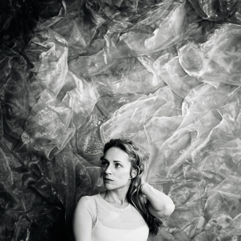 Agnes Obel liegt im hellen Licht auf geknitterter Folie und blickt nachdenklich zur Seite.