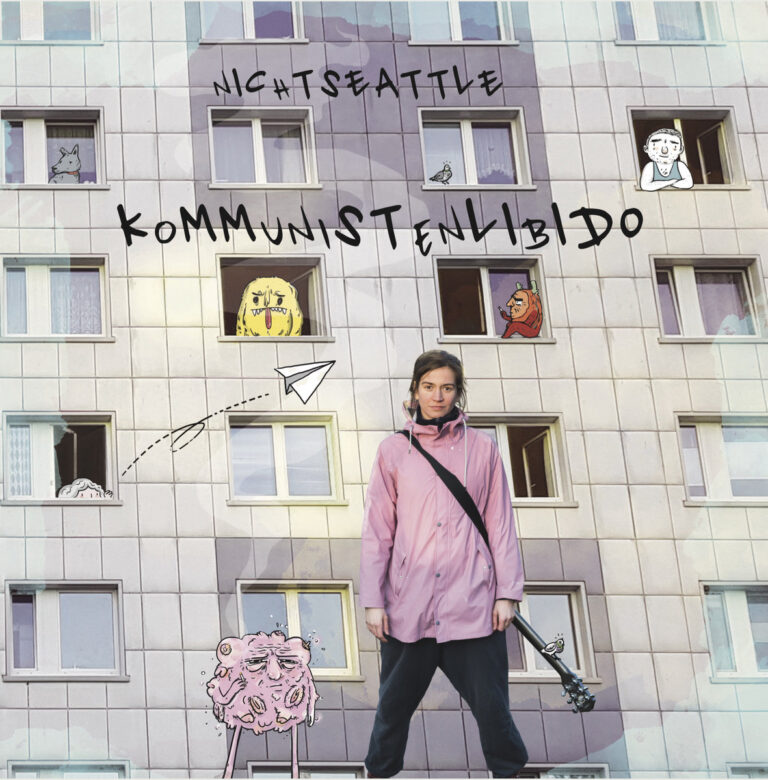 Katharina Kollmann steht in einer rosa Jacke vor einer Plattenbaufassade mit gezeichneten Figuren in den Fenstern.